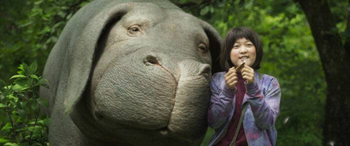 Image of Mija (Ahn Seo-Hyun) blowing a dandelion and Okja pressing her face against Mija's shoulder.